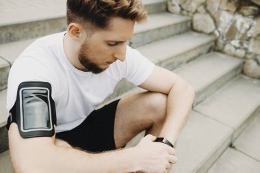 Göl kenarındaki sabahları çalıştırmadan önce spor saati ayarlama merdivenlerde oturan bir yakışıklı beyaz adam portresi kapatın.