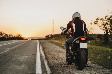 Onun motosiklet üzerinde oturan ve yaptığı gezi yolun yakınlarında başlayan şaşırtıcı bir beyaz gezgin arkadan görünüm.