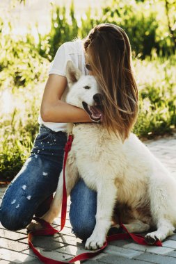 Köpeğini kucaklayan ve parkta kapalı gözlerle gülümser başında o süre öpüşme güzel uzun saçlı kız.
