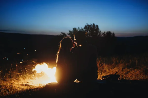 一对美丽的年轻夫妇坐在地面附近的火在晚上的时间和期待彼此旅行在他们的假期时间的侧面视图的肖像 — 图库照片