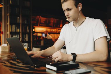 Yakışıklı genç erkek beyaz gömlek ve dikkatle ahşap masa üstünde laptop turuncu lambalar ile arka plan bulanık bakarak kulaklık görünümünü kırpma