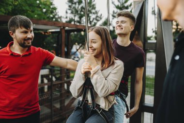 Mutlu genç adam kadın asılı ve personel erkeklerle zip hattını gezisine hazırlanıyor Emanet koşum ekipman