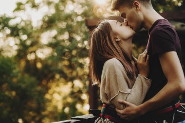 ZIP hat sürme vites giyen ve yaz Park ayakta iken güneş ışığında genç ihale çift öpüşme yan görünüm