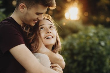 Mutlu bir adam ve şefkatle kucaklayan ve birbirlerine karşı güneş ışığı yeşil yaz parkta duran bakarak kadın