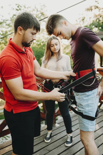 Adam genç adam yakın duran ve ZIP satır binmek için hazırlama kadın ile emniyet kemeri ile yardım yan görünüm
