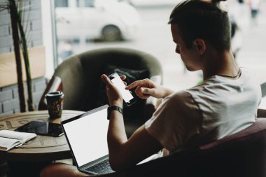 Yan görünüm genç adam laptop oturma ve smartphone kafede tarama 