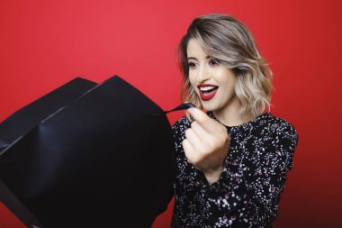 Kırmızı zemin üzerine siyah açılan Kağıt alışveriş çantası bakarak bluz parlak kırmızı dudaklar genç çekici kadın