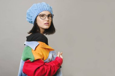 Şapka ve gözlük gri arka plan üzerinde renkli ceket kapalı alarak genç kadın yan görünüm 