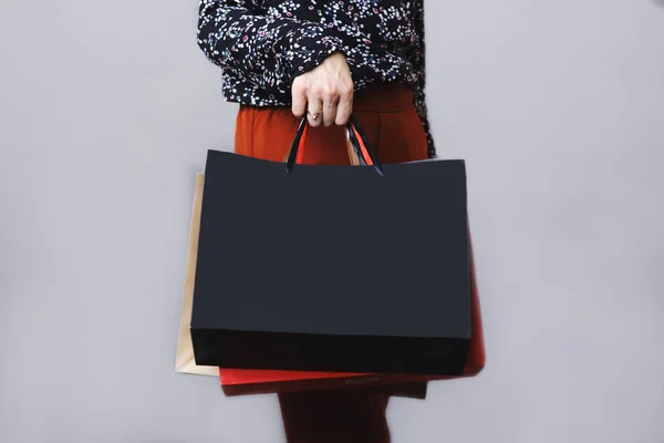 Crop side view of woman in blouse and terracotta trousers standing with paper shopping bags in hand isolated on gray background