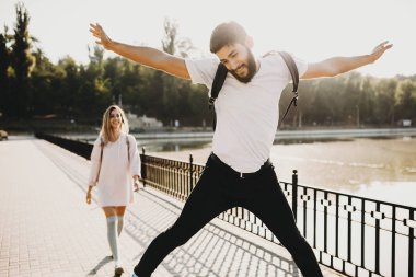 Sakallı adam kadın güneş ışığı ile promenade üzerinde yürürken yerden atlama sırt çantası ile heyecanlı