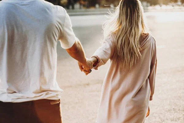 カジュアルなカップルは手を繋いでいると日差しの中で道を歩いての背面ビューのトリミング — ストック写真
