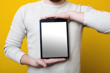 Modern tablet boş ekran ile tutarak ve parlak sarı zemin üzerinde dururken kamera için gösterilen tanınmayan erkek
