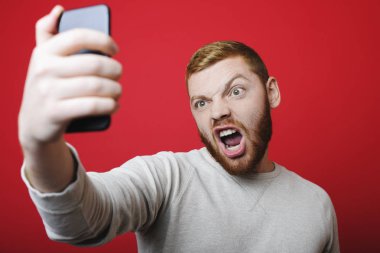 Selfie kırmızı arka plan üzerinde için poz süre kızgın surat kızıl sakallı yakışıklı genç adam