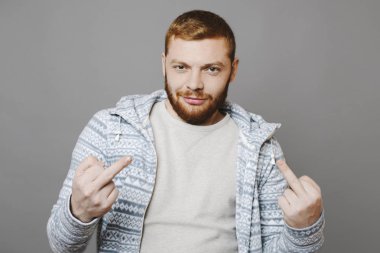 Kızıl saçlı adam sırıtışları ve gri arka plan ve jest siktir gösteren dururken kamera bakıyor
