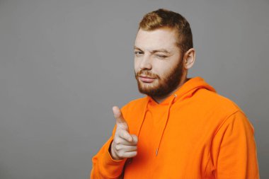 Göz kırpıyor ve gri arka plan üzerinde dururken kamera işaret turuncu hoodie yakışıklı adam