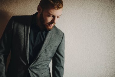 Kırmızı sakallı adam şık takım elbise uzak duran gri duvarının yakınında arıyor.