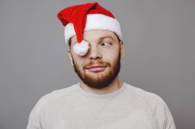 Gülümseyen ve uzak duran gri arka plan üzerinde seyir tatlı Noel şapkalı yakışıklı kırmızı sakallı adamı