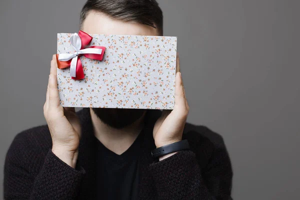 Anonymous guy hiding face behind lovely present while standing on gray background