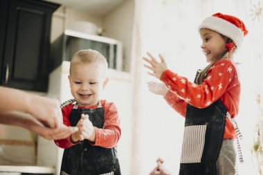 Noel Baba şapkası anne ile çerezleri Noel için yaparken elleri alkışlar un ile oynarken içinde yürümeye başlayan çocuk erkek ve kız çocuk gülüyor 