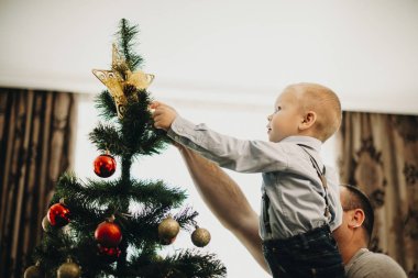 Yan görünümü şirin küçük çocuk ve tanınmayan adam Noel ağacı evde koyarak yıldız 