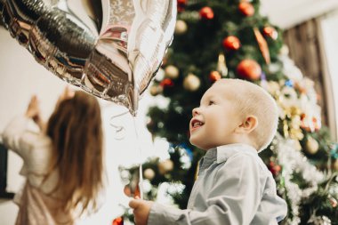 Aşağıdan gümüş balon evde parlak Noel ağacına arka plan ayakta tutan hayran yürümeye başlayan çocuk