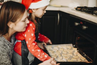 Yan görünümü pan koymak için kızı için yardım Anne mutfak ocakta kurabiye dolu 