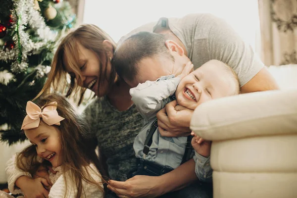 幸せな男と女を抱きしめるとキス愛らしい子供一緒に自宅のクリスマス ツリーのそばに座って — ストック写真