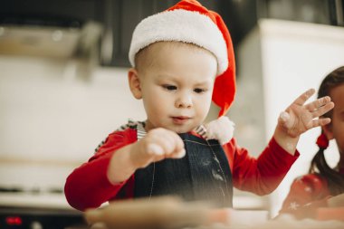 Noel Baba şapkası ile önlük giyen ve masada kurabiye hamur ve zemin ayakta yapmak bebek çocuk konsantre