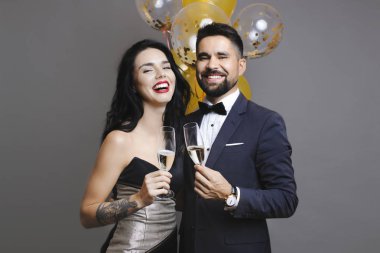 Yakışıklı erkek ve bardak şampanya tutarak ve balonlar gri arka plan üzerinde yakın dururken gülüyor şık kıyafetler içinde güzel kadın
