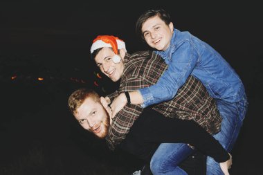 Gülümseyen ve eğlenirken sırasında kırsalında karanlık gece Noel kutlamaları kameraya bakarak gündelik kıyafeti üç genç adam yan görünüm