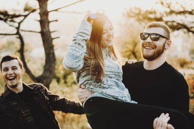 Gülümseyen ve büyüleyici kadın neşeli arkadaş yakınındaki doğada dururken kollarında taşıyan sakallı yakışıklı