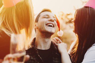 Grup gülümseyen genç insanlar ve tungur gözlük ve şişe alkol duran parlak güneşin karşı harika kırsal kesimde