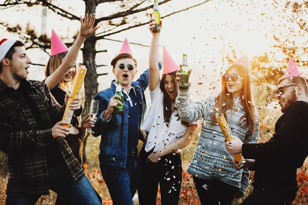Young people with beer screaming and exploding party crackers while celebrating Christmas in nature