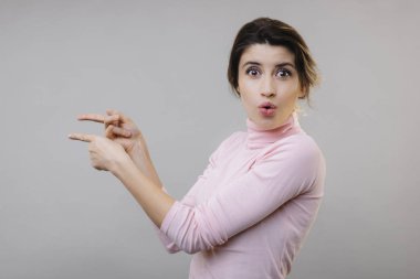 Yan görünüm güzel genç bayan bluz gösteren parmak tarafı ve kameraya gri arka plan üzerinde seyir için hayran