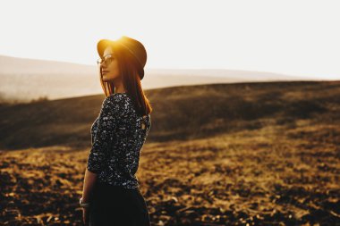 Şık kıyafet uzak harika gün batımı sırasında sonbahar alanındaki dururken bakan genç ve güzel kadın yan görünüm. Akşam alanında duran güzel kadın