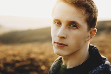 Kamera güneşli doğanın bulanık arka plan üzerinde dururken bakarak yakışıklı delikanlı. Kırsal kesimde genç adam