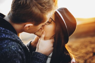 Genç adam tutkuyla dururken güzel kız arkadaşını bulanık arka plan doğa günbatımı sırasında öpüşme. Genç çift kırsal kesimde öpüşme