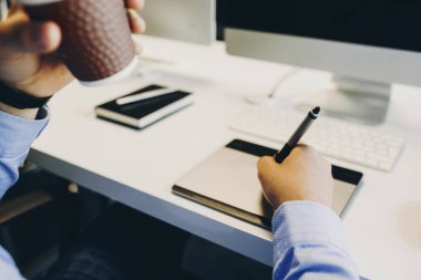 Sıcak içecek keyfi ve ofis masa başında otururken grafik tablet üzerinde çizim tanınmayan adam. Tasarımcı içme ve grafik tablet kullanarak kırpma