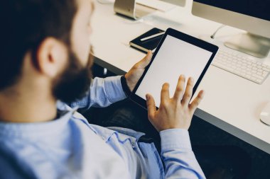 Kırpma modern ofis masasında otururken modern tablet boş ekran dokunaklı adam sakallı. Tablet kullanarak anonim ofis çalışanı