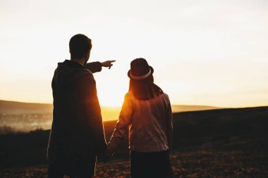 Arka görünümü elele ve alandaki dururken muhteşem gün batımı manzarasına hayran kadın ve genç adam. Tanınmayan çift batımını