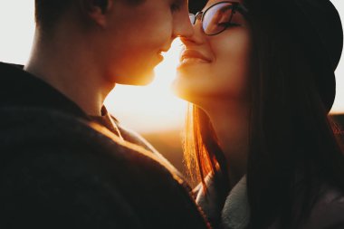 Yakışıklı genç ve güzel kadın gülümseyerek ve burun kırsal gökyüzünde gün batımına karşı dururken dokunmadan yan görünüm. Genç çift burun günbatımı sırasında dokunmadan