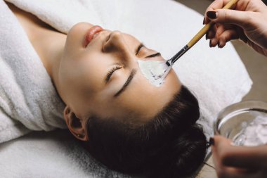 Hyaluronik asit ile beyaz bir maske yapıyor bir spa prosedürler sahip şirin genç kadın.