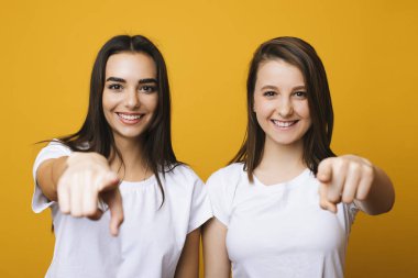 İki güzel genç kız kameraya bakarak ve kameraya gülümseyen sarı duvara onların parmak ile işaret arıyorum portresi. Sana onun parmakları ile işaret iki kız arkadaşım.