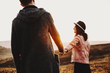 Güzel Avrupa çift gündoğumu karşı ellerini tutarak seyahat. Uzakta onların tarih saat seyahat ederken erkek arkadaşı eliyle tutarak gülümseyen güzel kız arıyor.