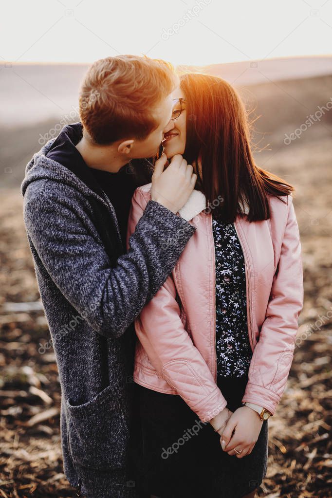 Amazing portrait of lovely caucasian couple kissing while man is touching her face against beautiful sunset light while traveling.