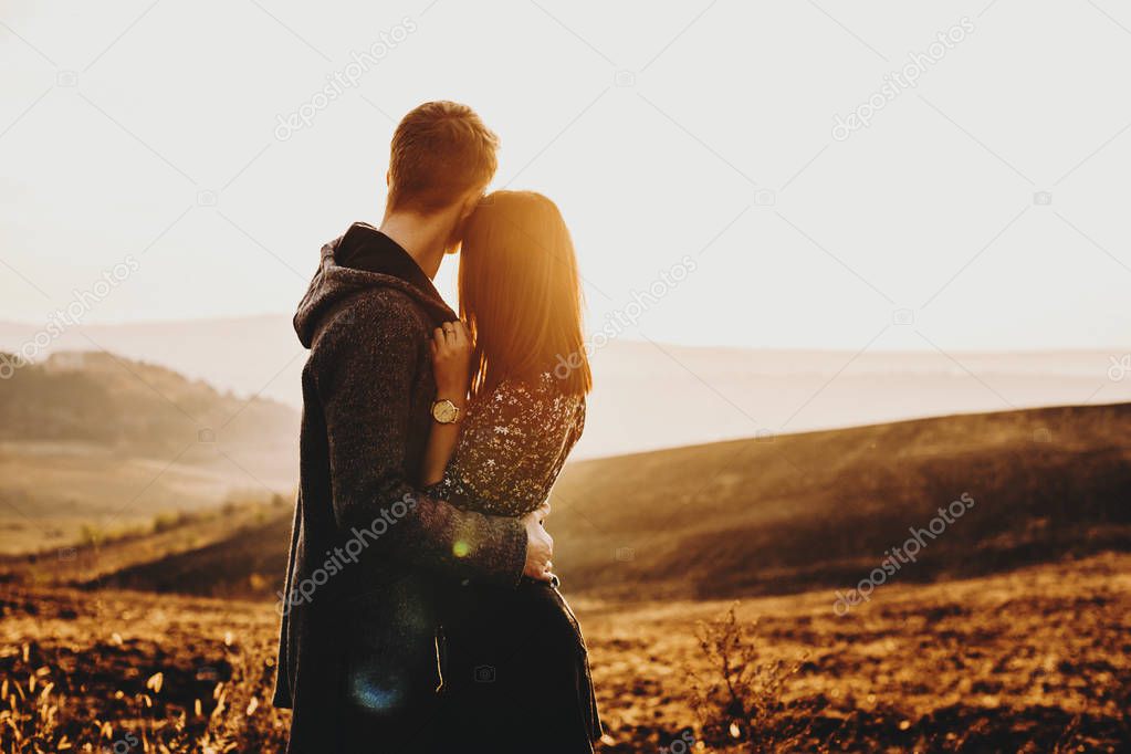Adorable young caucasian couple hugging and looking away at the epic view dreaming at the sunset in their vacation time.
