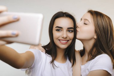İki güzel kız arkadaşım başka bir beyaz arka plan önünde kafasına öpüyor selfie gülümseyerek yapıyor.