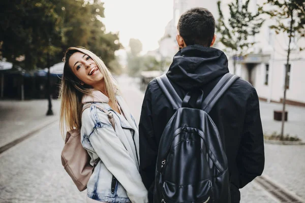 Úžasný Pár Nosí Batohy Zatímco Dívka Při Pohledu Kamery Ukazuje — Stock fotografie