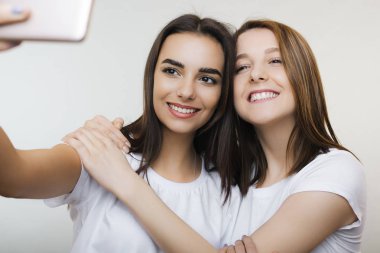 İki güzel genç kadın bir selfie yapıyor ve gülüyor sarılma beyaz bir arka plan beyaz gömlek giymiş.