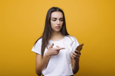 Sevimli genç beyaz kadın onu smartphone ve gösteri sarı bir arka plan önünde de parmak ile sürpriz arıyor.